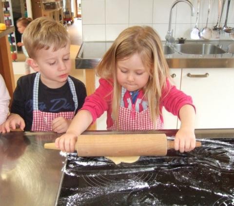 Zwei Kinder rollen in der Küche ein Stück Teig mit einem Nudelholz aus