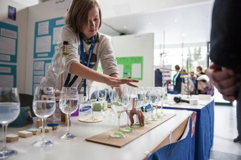 Schülerin zeigt beim Wettbewerb ihr Experiment mit Weingläsern, die unterschiedlich hoch mit Wasser gefüllt sind