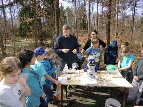 Eine Gruppe von Kindern schaut mit Thomas Peissner durch das Mikroskop.