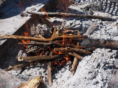 Grillstelle mit Holzstöcken, kleinen Flammen und Asche