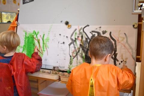 Zwei Kinder stehen an der Staffelei und malen mit Wasserfarben 