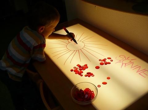 Ein Kind arbeitet an einem Leuchttisch mit einem Stift und Legematerial