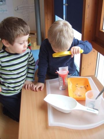 Zwei Kinder sitzen an einem Tisch und beobachten mit einer Lupe wie Wasser durch einen Filter fließt