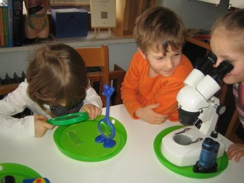 Drei KInder untersuchen Objekte mit Lupe und Mikroskop