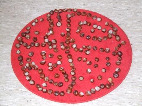 Auf einem roten, runden Teppich liegt ein Ornament aus Kastanien