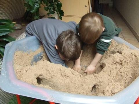 Zwei Kinder graben mit den Händen in einer mit Sand gefüllten Wanne
