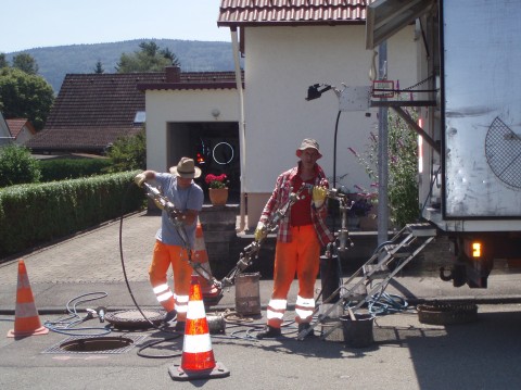 Zwei Männer sanieren einen Kanal mit Hilfe der entsprechenden Werkzeuge. Sie stehen neben einem Betriebsfahrzeug