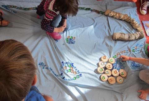 Kinder legen auf einem Bodentuch aus diversen Materialien Schneckenbilder