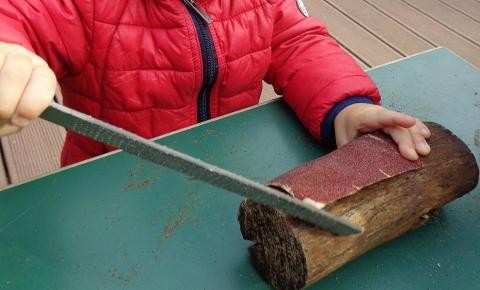 Kinderhände - ein Holzklotz wird mit Schmirgelpapier und einer Raspel bearbeitet