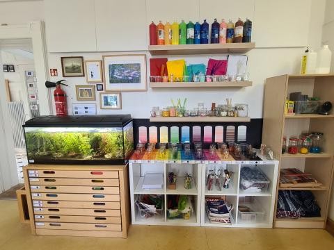 Ein Aquarium, verschiedene Bastel- und Malmaterialien, die nach den Regenbogenfarben sortiert sind.