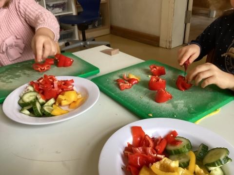 Kinderhände schneiden mit einem Messer rote Paprika.