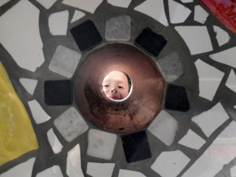 Ein Kind schaut durch das Loch einer Säule.
