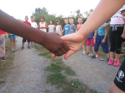Zwei Kinder reichen sich die Hände. Im Hintergrund ist zu sehen, dass die Kinder in einem Kreis zusammen stehen.