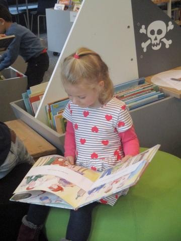Ein Kind sitzt auf einem grünen Hocker in der Stadtbibliothek Sindelfingen und schaut sich ein Bilderbuch an 
