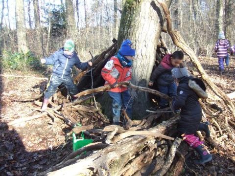 Mehrere Kinder stehen im Wald und stellen Äste zu einem Zelt zusammen